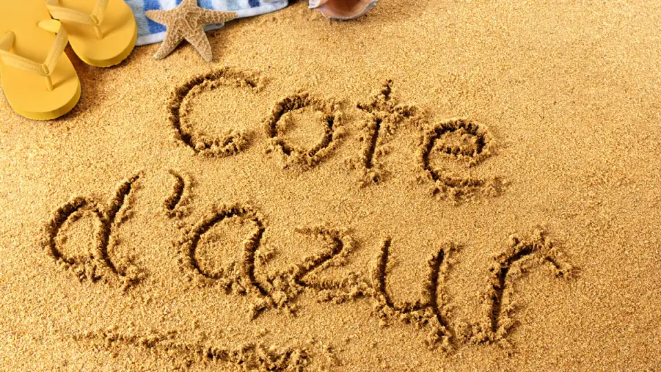 Côte d’Azur écrit dans le sable d’une plage, à côté de tongs jaunes et d’une étoile de mer
